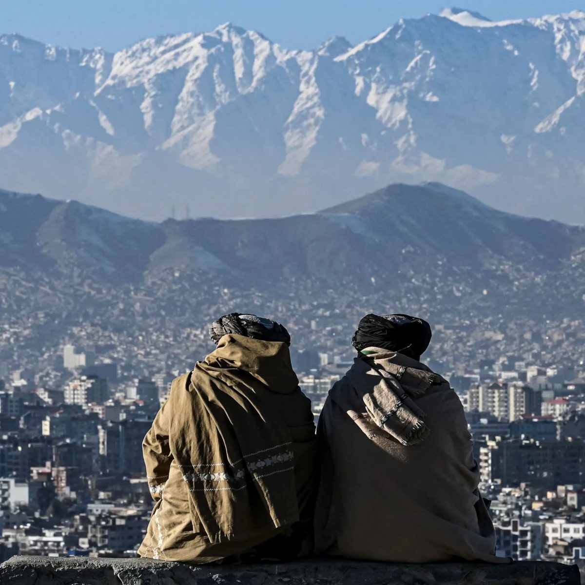 AFP via Getty Images Photo d'archive montre deux membres des talibans assis regardant la ville de Kaboul, avec des montagnes en arrière-plan, tournés de dos, à la caméra, prise sur la colline Wazir Akbar Khan en janvier 2022.