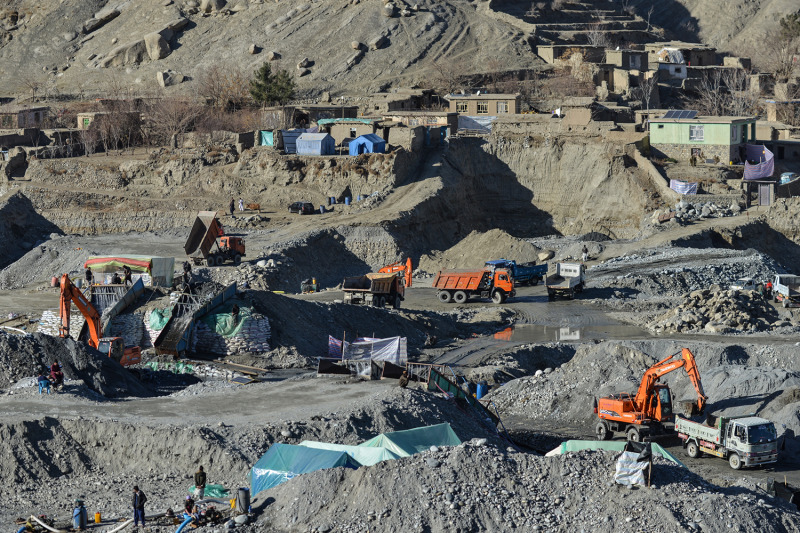 Des ouvriers et des équipements de construction sont aperçus de loin dans un paysage lunaire, cratérisé, déchiré par l'activité minière. Sur une crête au loin se trouvent quelques tentes et des bâtiments simples d'un étage.